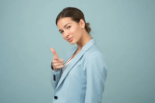 A stock photo of a female manager displaying casual confidence by pointing her hand like a gun.